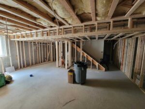 A worker examines a basement foundation wall with a moisture meter and flashlight.